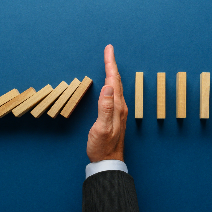 Suited hand between falling dominos and standing dominos, on teal blue background