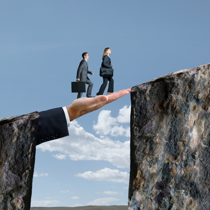 Two people in business suits with briefcases walking uphill across a gap in two mountains, they're walking across an outstretched hand/arm also in a suit